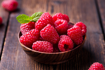 Ripe sweet raspberries in bowl on wooden table.