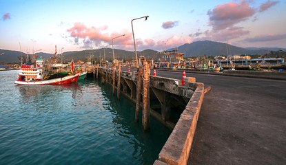 Fototapeta premium Landscape sea pier at sunset. The evening and the fishing boats reflecting in the dark water. Thailand, Koh Samui.