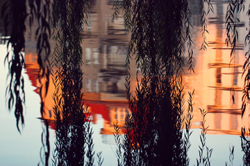 Brunches of willow touching a lake with a house reflected in the water.