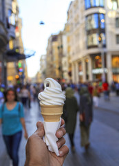 Hand holding vanilla ice cream, people in the street.