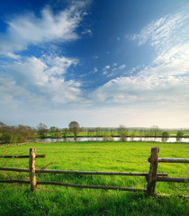 Spring Landscape of Green Meadow with Wooden Fence along River under Blue Sky © AVTG