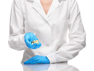 Doctor in white gown and gloves holding tablets and capsules