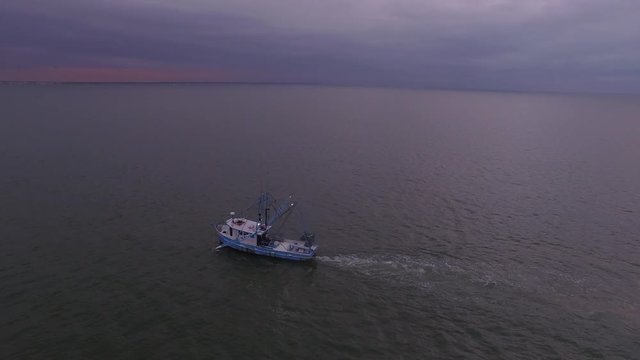 Aerial view of a shrimp boat trawling in open water in the Atlantic ocean, with colorful cloudy sky at dawn.