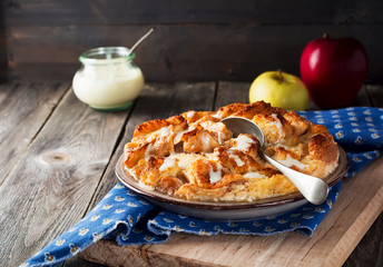 Bread pudding breakfast casserole with apples and vanilla sauce on the old wooden background. Selective focus.