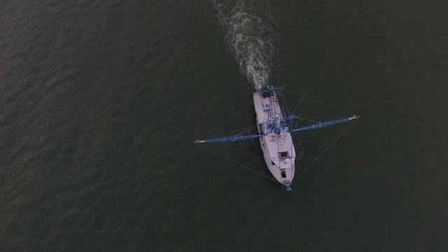 Aerial view of a shrimp boat trawling in open water in the Atlantic ocean, with colorful cloudy sky at dawn.