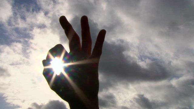 Hand rising into frame to give an a-okay sign with sun shining through then covers frame to black, concept.