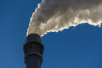 rauchender Industrie Schornstein, weißgraue Abgaswolke aus Schlot auf blauem Hintergund / Himmel