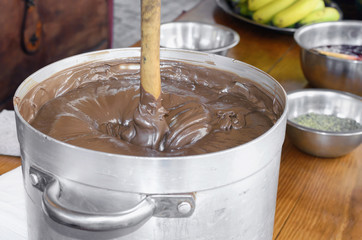 Big casserole of chocolate with milk. At the background some fruits like Canarian bananas and other spices for making desserts and candys. Medieval stall. Village's food.