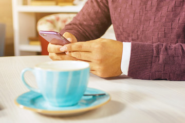 Young man holding a mobile phone and smiling. Read the posts and drinking coffee.