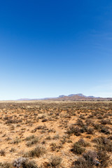 Plakat Portrait - Barren field with mountains and blue sky