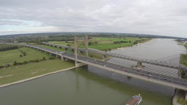 Aerial of briges with traffic moving over and barge transport ship moving underneath it on the cable-stayed bridge a highway is running over on smaller bridge a railroad over river steady flight 4k