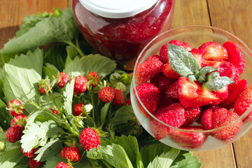 strawberries in transparent bowl and bunches with leaves
