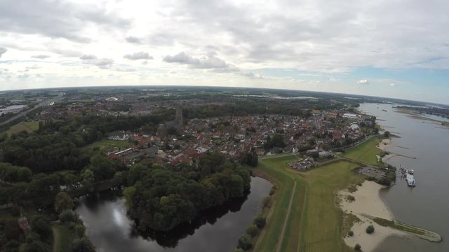 Aerial footage of a small town in Holland the Netherlands located near a river showing buildings small part of beach and also the side of river and some smaller boats at shore overcast weather 4k
