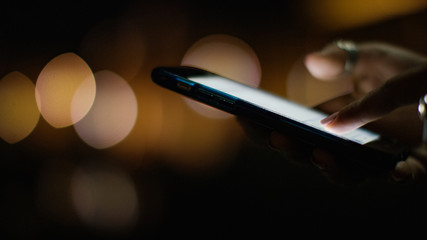 Close up of a female hand using a phone at night with a blurred lights background