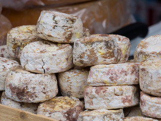 Group of Natural mountain cheeses with mold on rind exposed in a wooden box during a country fair
