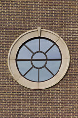 Portal style window on brick wall with clear blue sky reflected in window.
