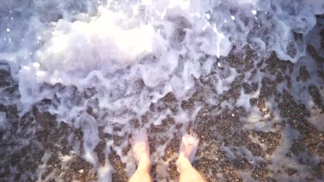 Man feet washed by sea waves and buries them in the sand. Top view.
