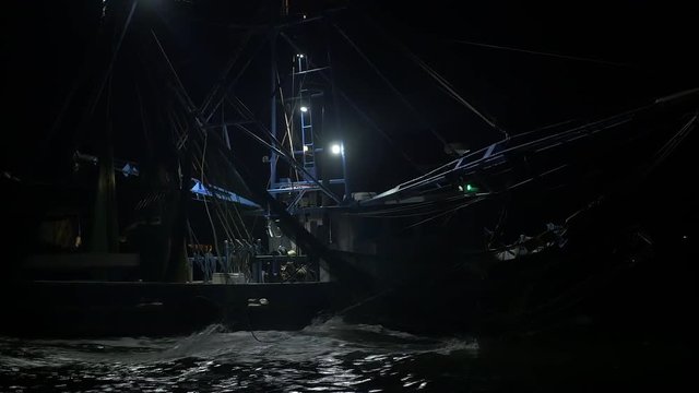 Pan up on shrimping trawler sailing out to sea to fish at night.