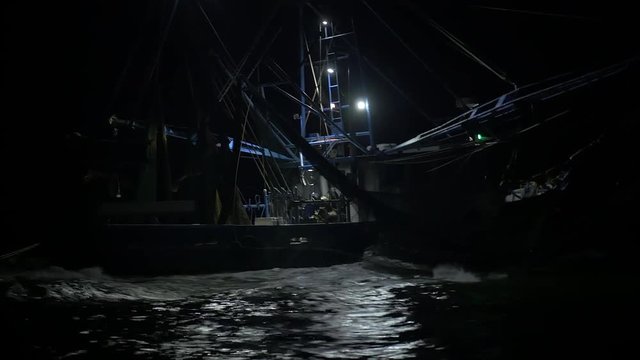 Pan up on shrimping trawler sailing out to sea to fish at night.