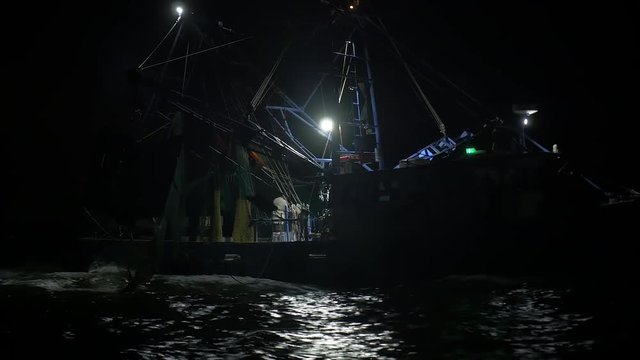 Shrimping trawler sails out to sea at night to fish with its nets down.
