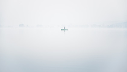 Alone fisherman on the boat in a thick fog on the lake on an autumn morning in calm weather