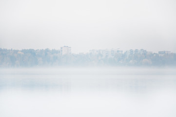 Heavy fog on the lake Senezh in Solnechnogorsk fall in calm weather. View of the residential high-rise buildings through the haze. Autumn morning water landscape