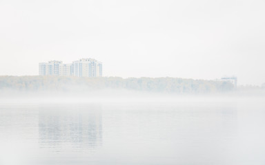 Heavy fog on the lake Senezh in Solnechnogorsk fall in calm weather. View of the residential high-rise buildings through the haze. Autumn morning water landscape