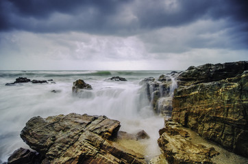 beautiful beach with rock hitting by waves. soft focus due to long exposure. dramatic dark clouds and rocky island