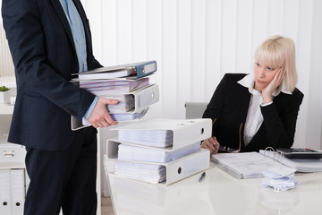 Businessman Giving Pile Of Folders To Female Assistant