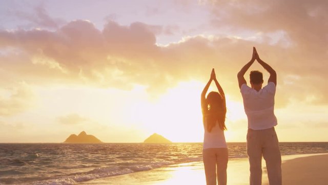 Yoga, fitness, sport, and wellness lifestyle concept. Couple doing yoga exercises on beach from back at sunrise on serene peaceful beach. Relaxation and yoga meditation on Lanikai, Oahu, Hawaii