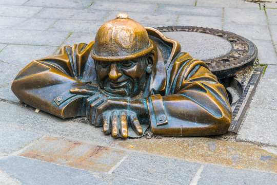 Cumil (The Watcher) statue of man peeking out from under a manhole cover in Bratislava, Slovakia.