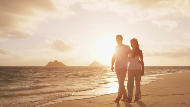 Romantic couple walking at beach at sunset embracing and holding hands. Young couple in love enjoying romance in casual elegant clothing on luxury beach vacation travel holidays, Lanikai, Oahu, Hawaii