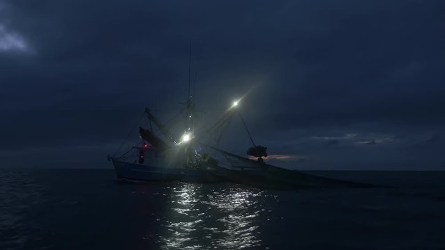 Shrimping trawler fishing at the first light of dawn with nets in the water.