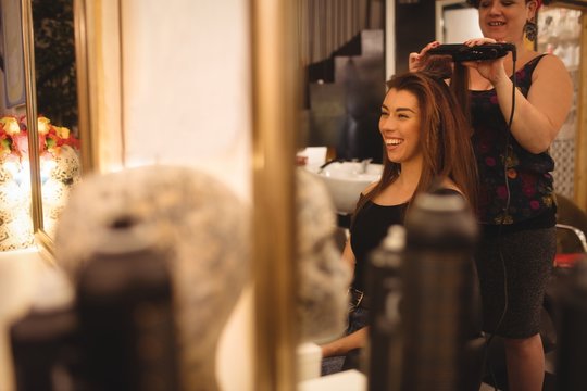 Woman smiling while getting her hair straightened in salon