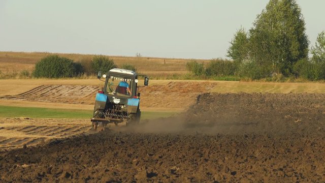 Farm tractor plowing the field, leaving behind a cloud of dust