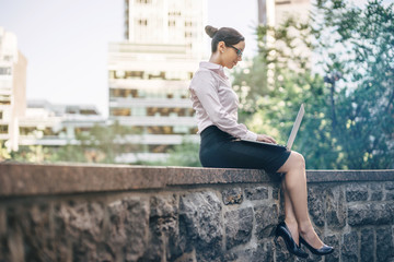 Photo business woman wearing white shirt and working on laptop outdoors, young professional business woman sitting outdoors and using laptop, businesswoman using laptop while working on new project.