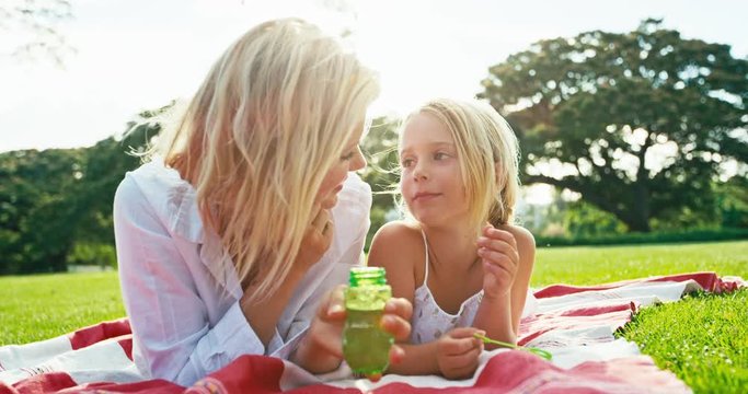 Mother and daughter relaxing together blowing bubbles in the park