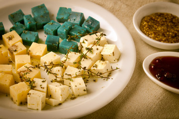 Cheese platter, Gouda, feta, blue pesto cheeses on white plate with herbs, olive oil, pomegranate and mustard sauces