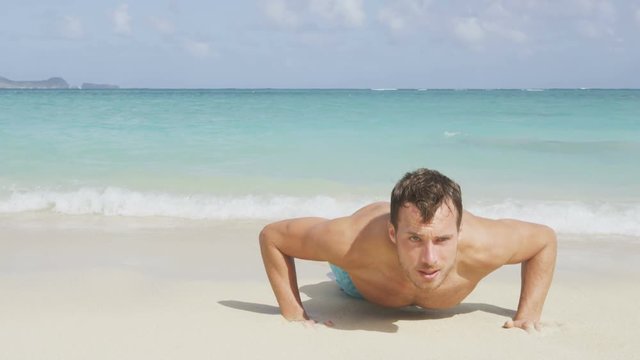 Fitness push-up crossfit man sport model training pushups on beach outdoors. Fit male fitness trainer working out exercising in summer on beach. RED EPIC SLOW MOTION, 96 FPS.