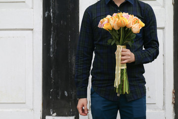Man holding a bouquet of flowers consisting of roses and tulips and standing against vintage door background