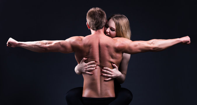 beautiful woman embracing and biting muscular man over grey