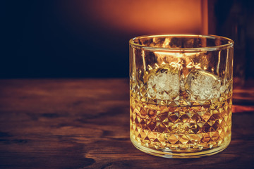 glass of whiskey with ice cubes near bottle on wood table, warm atmosphere