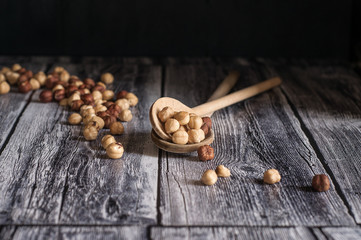 due cucchiai di legno sono pieni di nocciole tostate e altre sono sparse su base di legno. Fotografia orizzontale