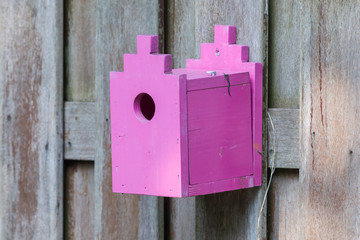 Pink birdhouse on a wooden fence