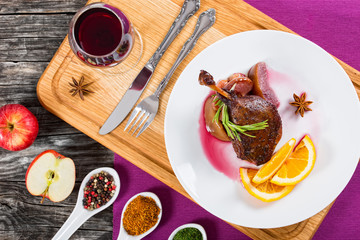 roasted duck leg on platter with glass of red wine