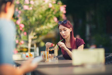 Young beautiful red hair woman drinking coffee in summer cafe ou