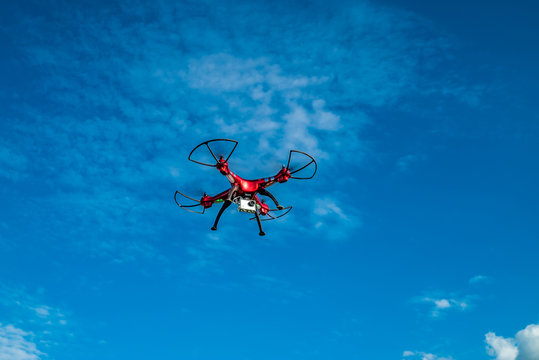Roter Quadrocopter unter weiß-blauem Himmel fliegt durch die Luft