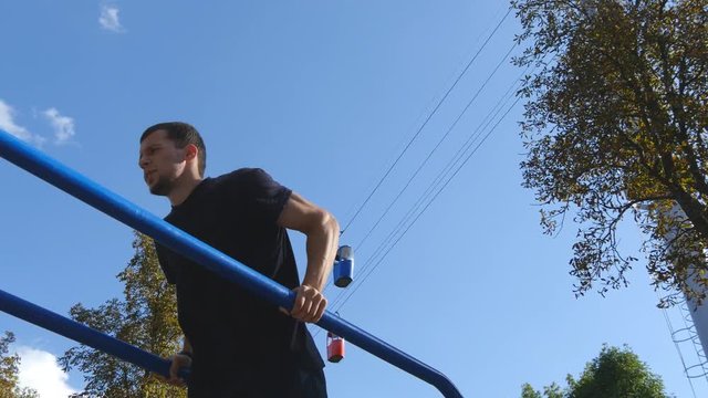 Athletic man doing push ups on parallel bars at sports ground in city park. Strong young muscular guy training outdoor in summer. Athlete exercising at playground. Workout healthy lifestyle. Closeup