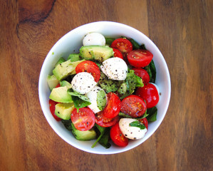 Fresh salad with avocado slices, cherry tomatoes and mozzarella. White bowl on a wooden table. High angle shot.