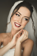 Beautiful young bride with makeup and hairstyle in bedroom, newlywed woman final preparation for wedding. Happy girl waiting groom. Portrait soft focus